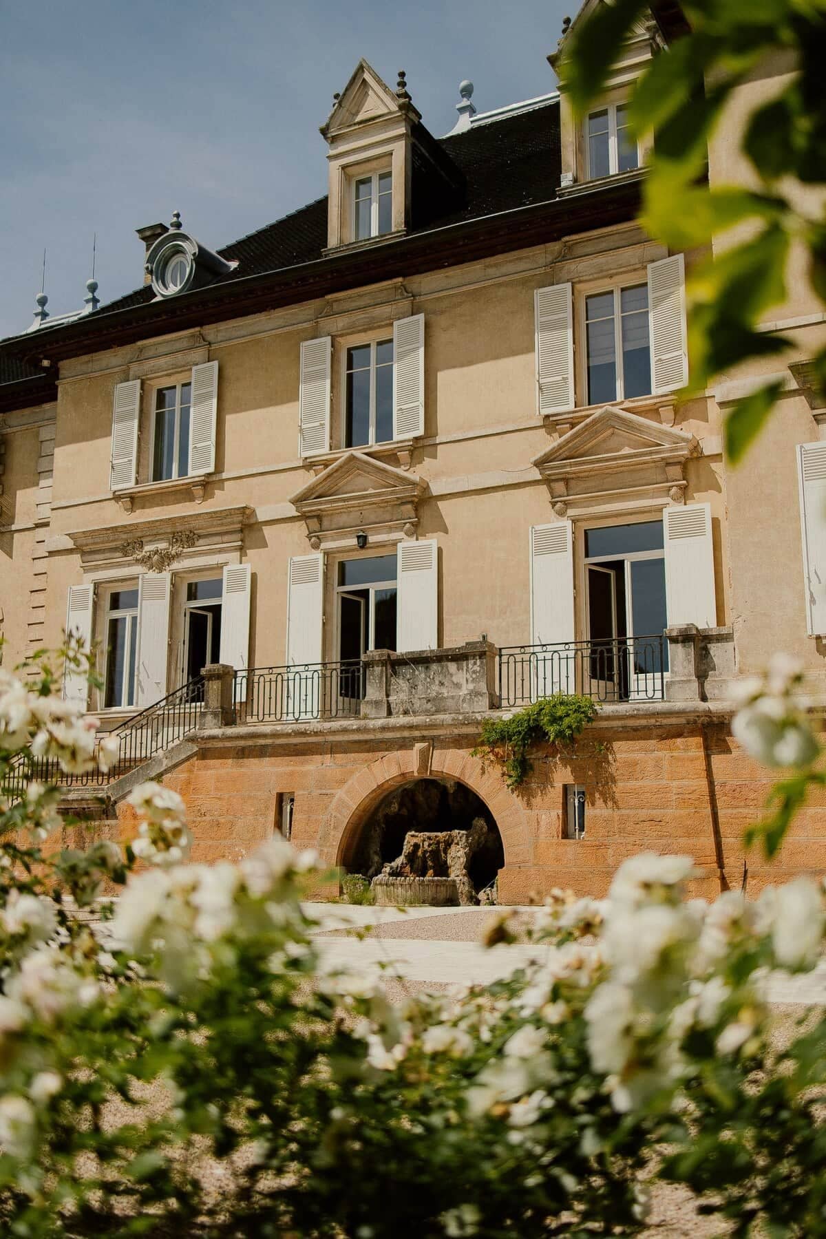 A multi-story building with a central entrance, a balcony with a railing, and a stone archway.