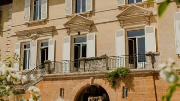 A multi-story building with a central entrance, a balcony with a railing, and a stone archway.
