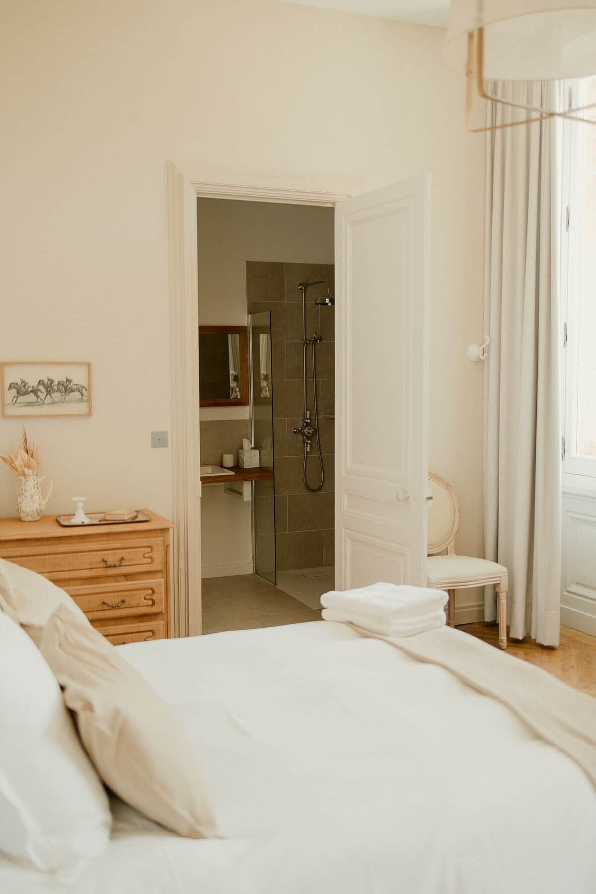 Een hotelkamer met een bed, een houten dressoir, een badkamer met douche en een stoel.