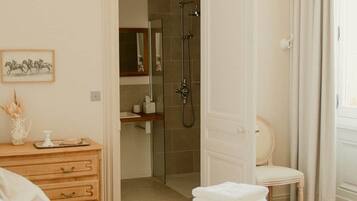 Een hotelkamer met een bed, een houten dressoir, een badkamer met douche en een stoel.