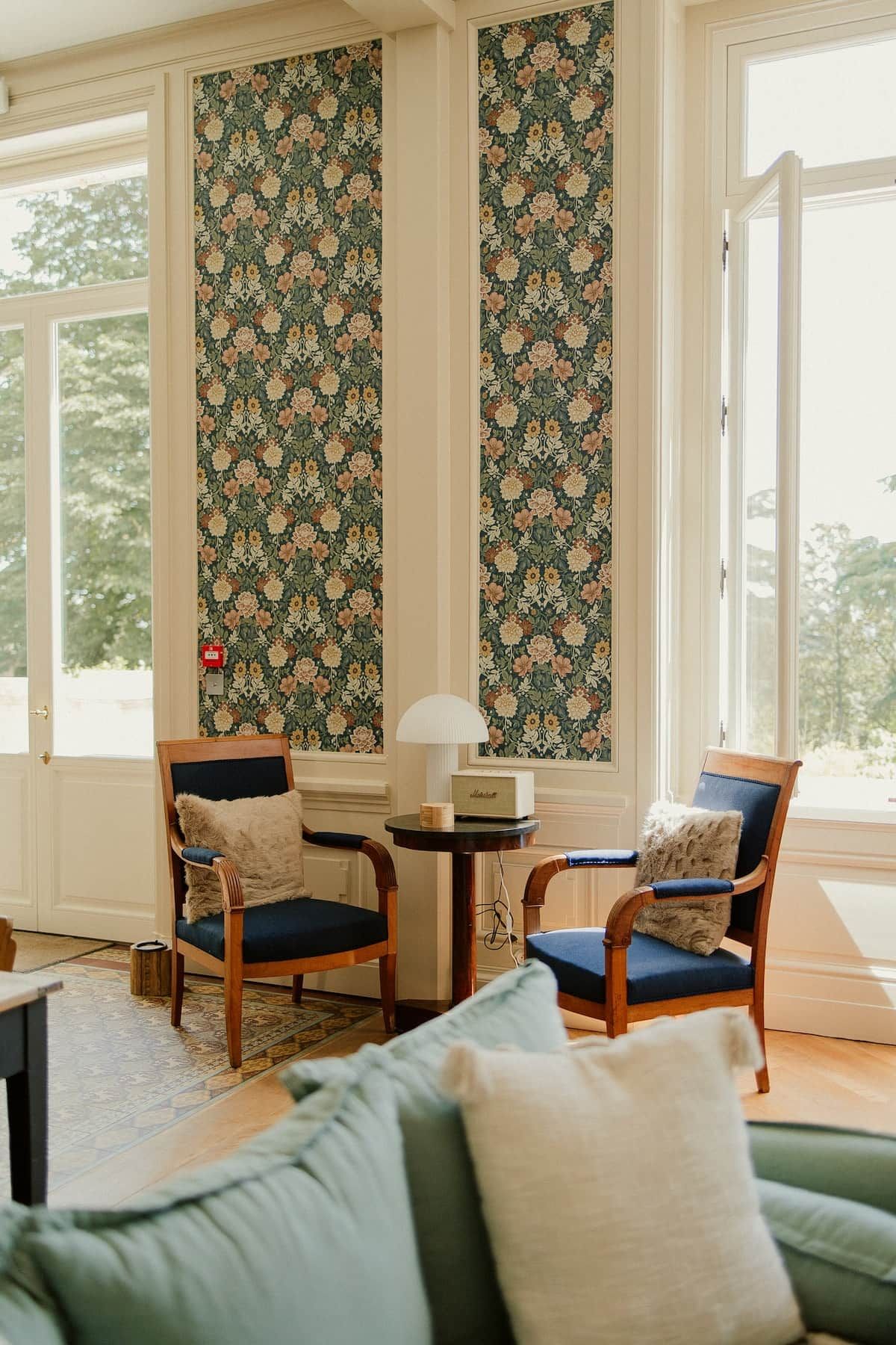 Une pièce avec deux chaises en bois, une petite table avec une lampe et un canapé vert.