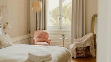 A bedroom with a large bed, a chair, a lamp, and a window with curtains.