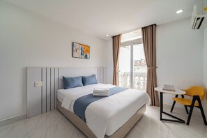 A hotel room with a bed, a painting, a window with curtains, a small table with a chair, and a sign indicating a non-smoking room. - Cozrum Homes - The Ivory House (Tan Hung)