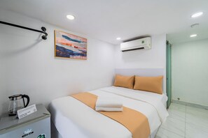 Quarto de hotel com cama, quadro, unidade de ar condicionado, chaleira e placa com texto.