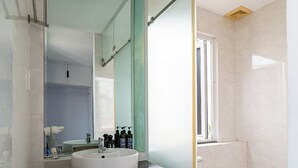A modern bathroom with a glass shower enclosure, a white toilet, and a sink with a black countertop. - Cozrum Homes - The Ivory House (Tan Hung)