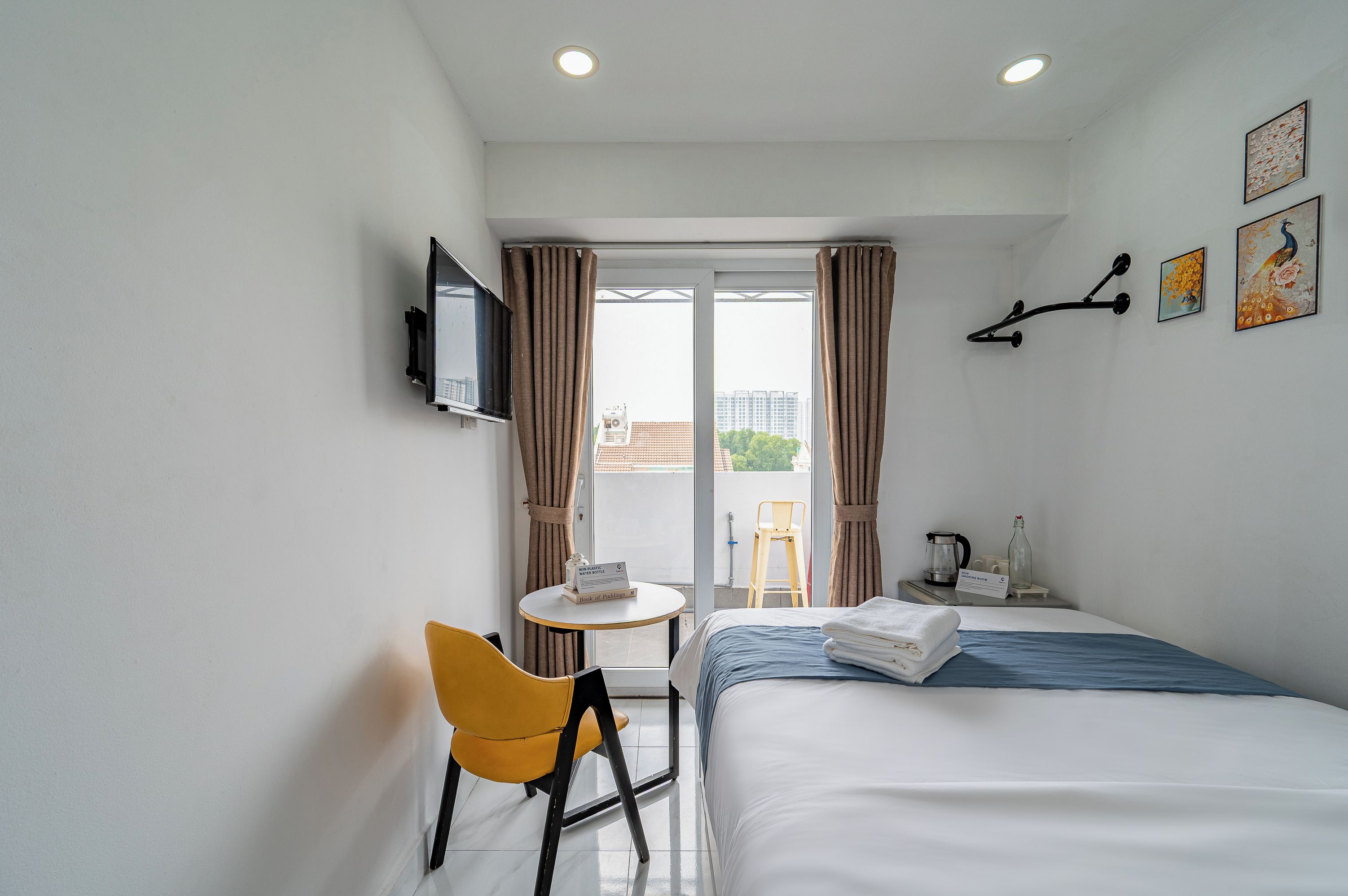 Habitación de hotel con cama, una silla, una mesita, televisor y balcón con vista a edificios.