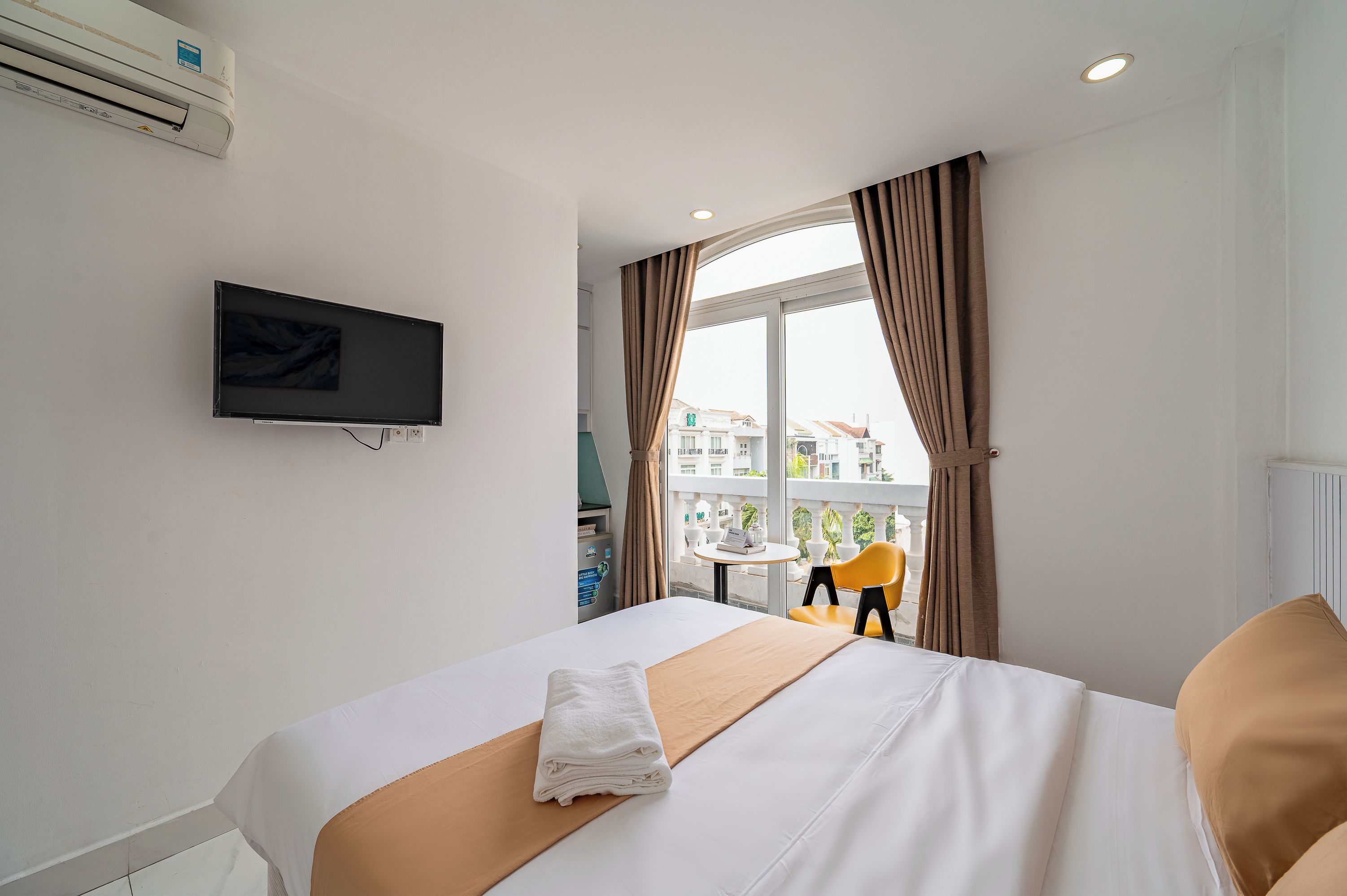 Una camera d'albergo con un letto, una televisione a muro e una finestra con tende.