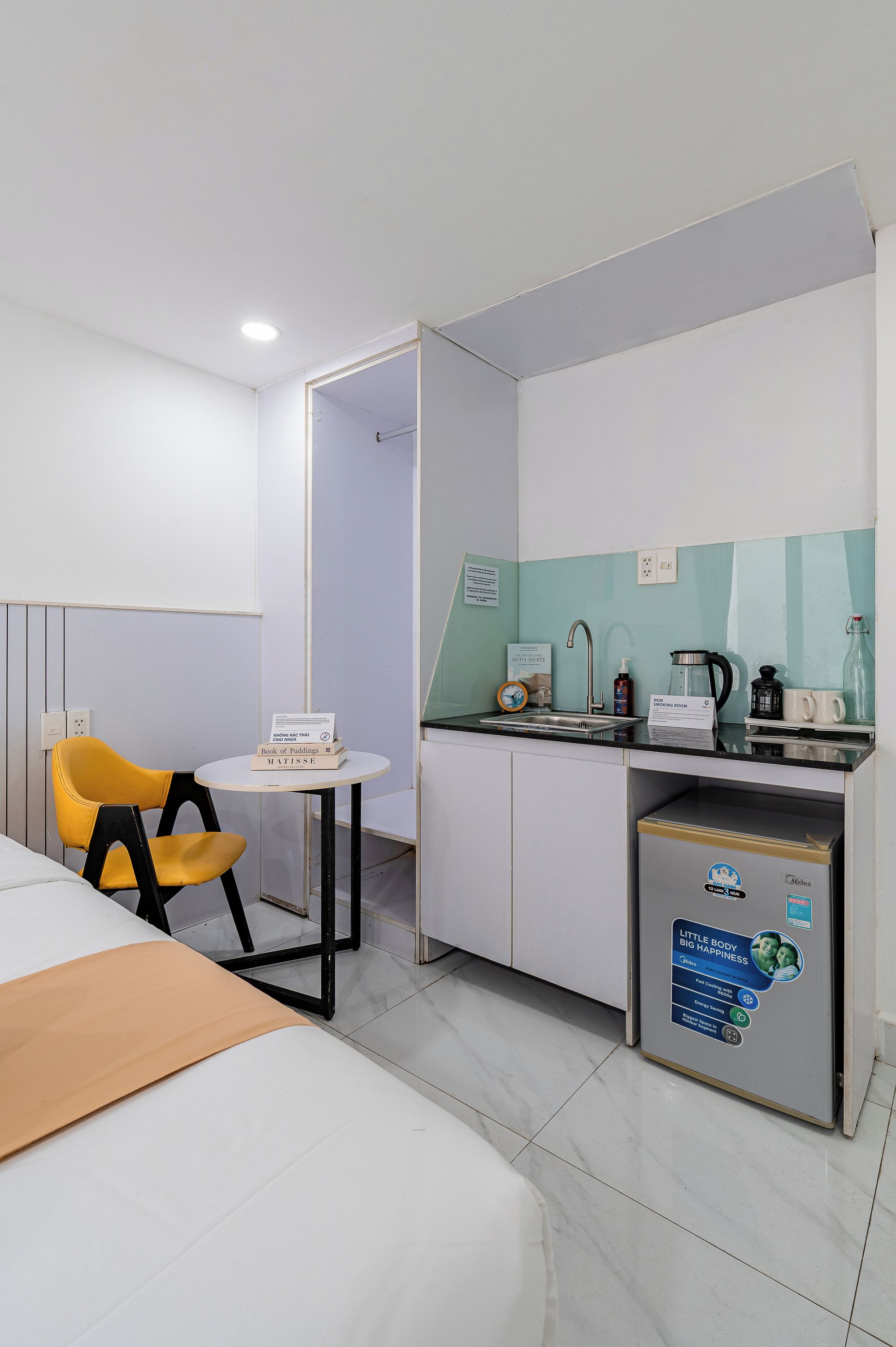 Habitación de hotel con cama, una mesita con una silla, kitchenette y baño visible a través de una puerta abierta.
