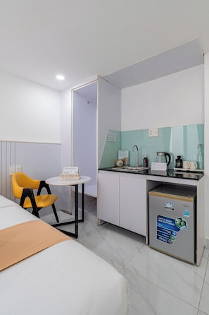 A hotel room with a bed, a small table with a chair, a kitchenette, and a bathroom visible through an open door. - Cozrum Homes - The Ivory House (Tan Hung)