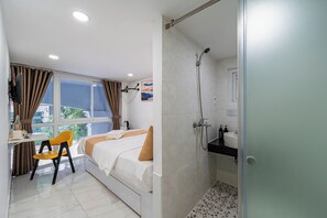 Habitació d'hotel amb llit, escriptori, cadira, zona de dutxa i vistes a l'exterior.
