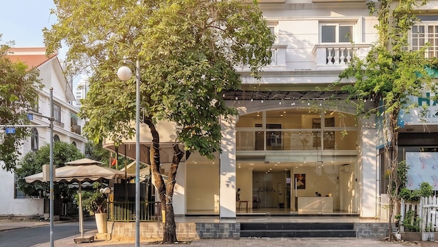 A multi-story building with a central entrance, balconies, and a tree in front. - Cozrum Homes - The Ivory House (Tan Hung)