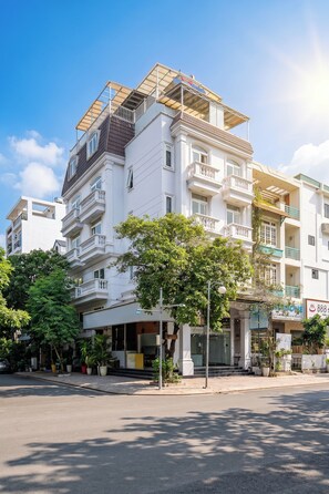Um edifício com várias andares, varandas, uma rua em frente e árvores.