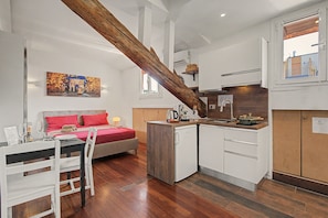 A compact hotel room with a bed, a small kitchenette, a dining area, and a wooden ceiling beam. - Apartment 'Piranesi 45' with Wi-Fi and Air Conditioning (Milano)