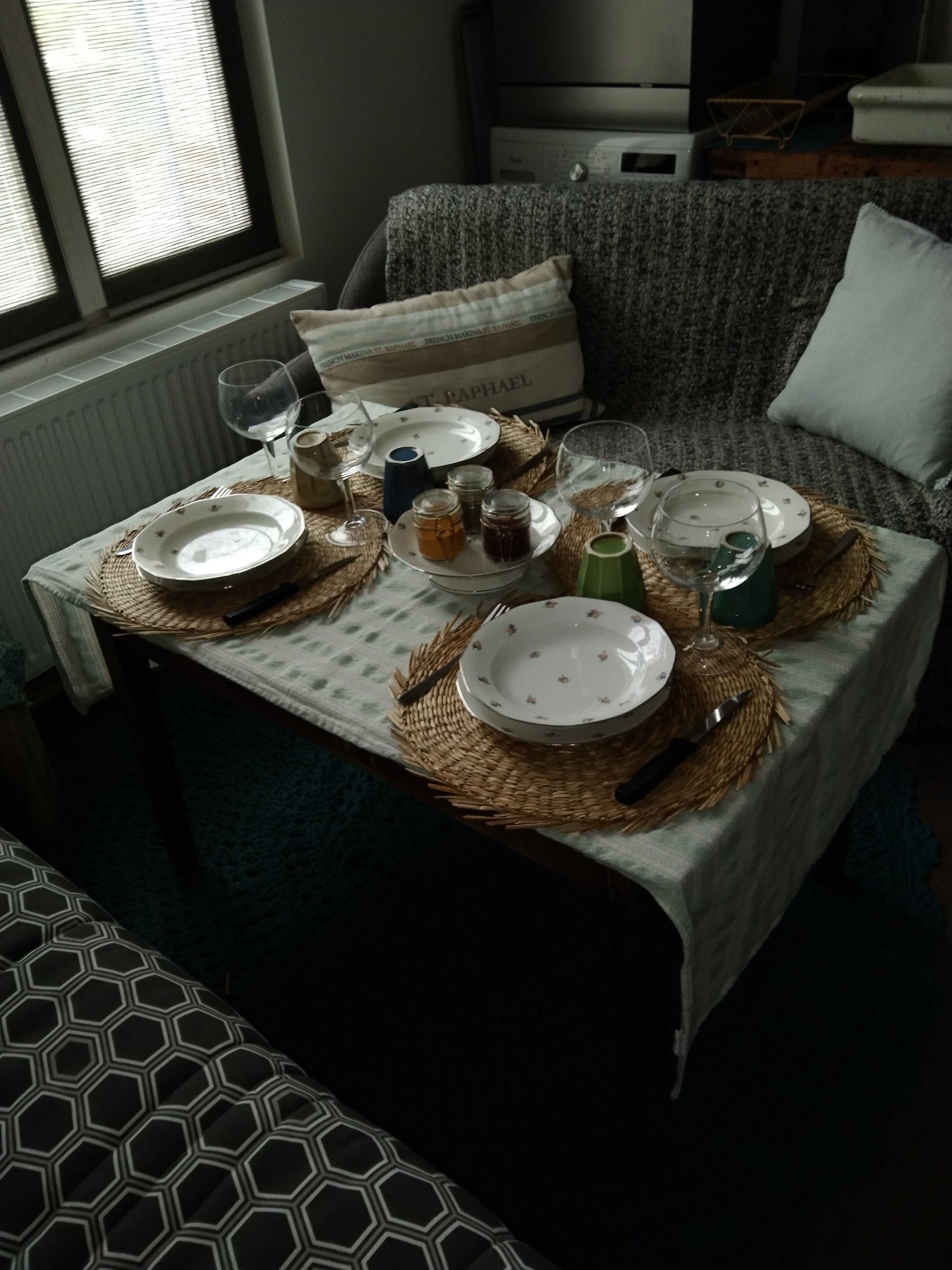 Une table à manger dressée avec des assiettes, des verres et des pots, entourée de sets de table en fibres tressées.