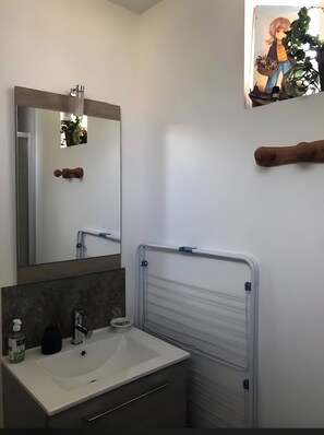 Een badkamer met een wit wastafelmeubel, een spiegel en een douchegedeelte.