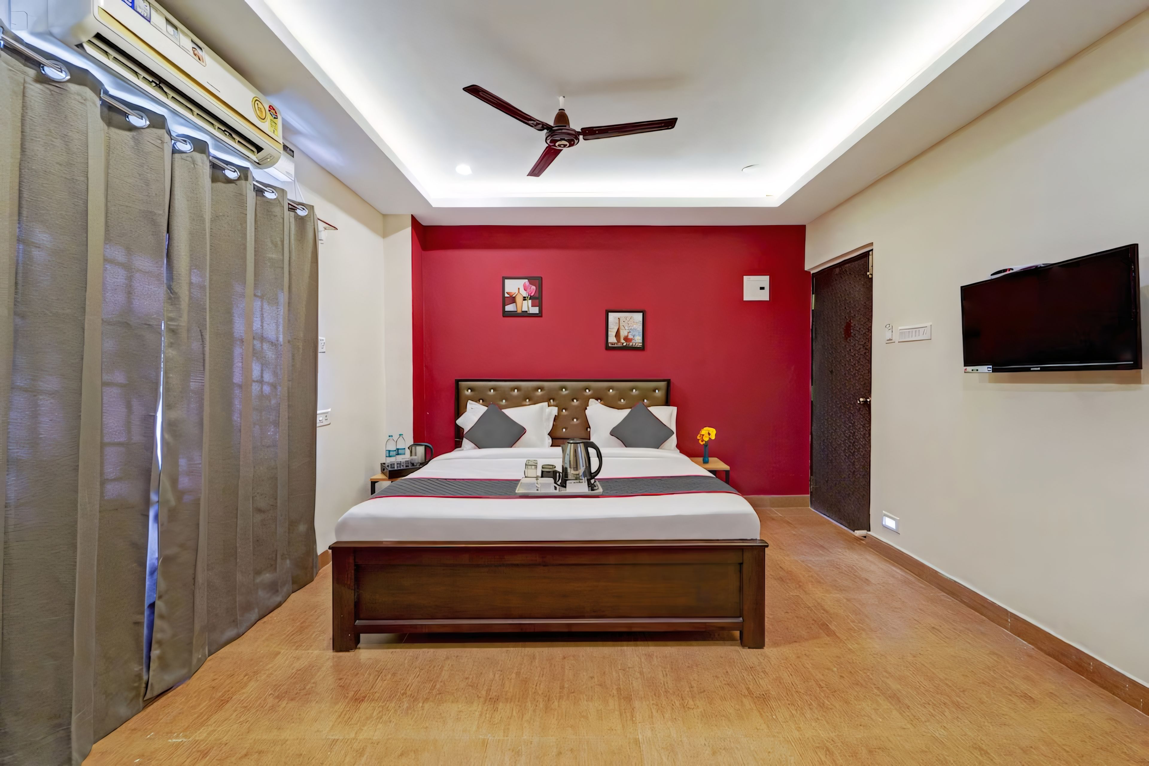 Habitación de hotel con cama, ventilador de techo, televisión y pared roja.