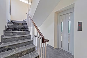 A staircase with marble steps and a wooden handrail leading to an elevator.