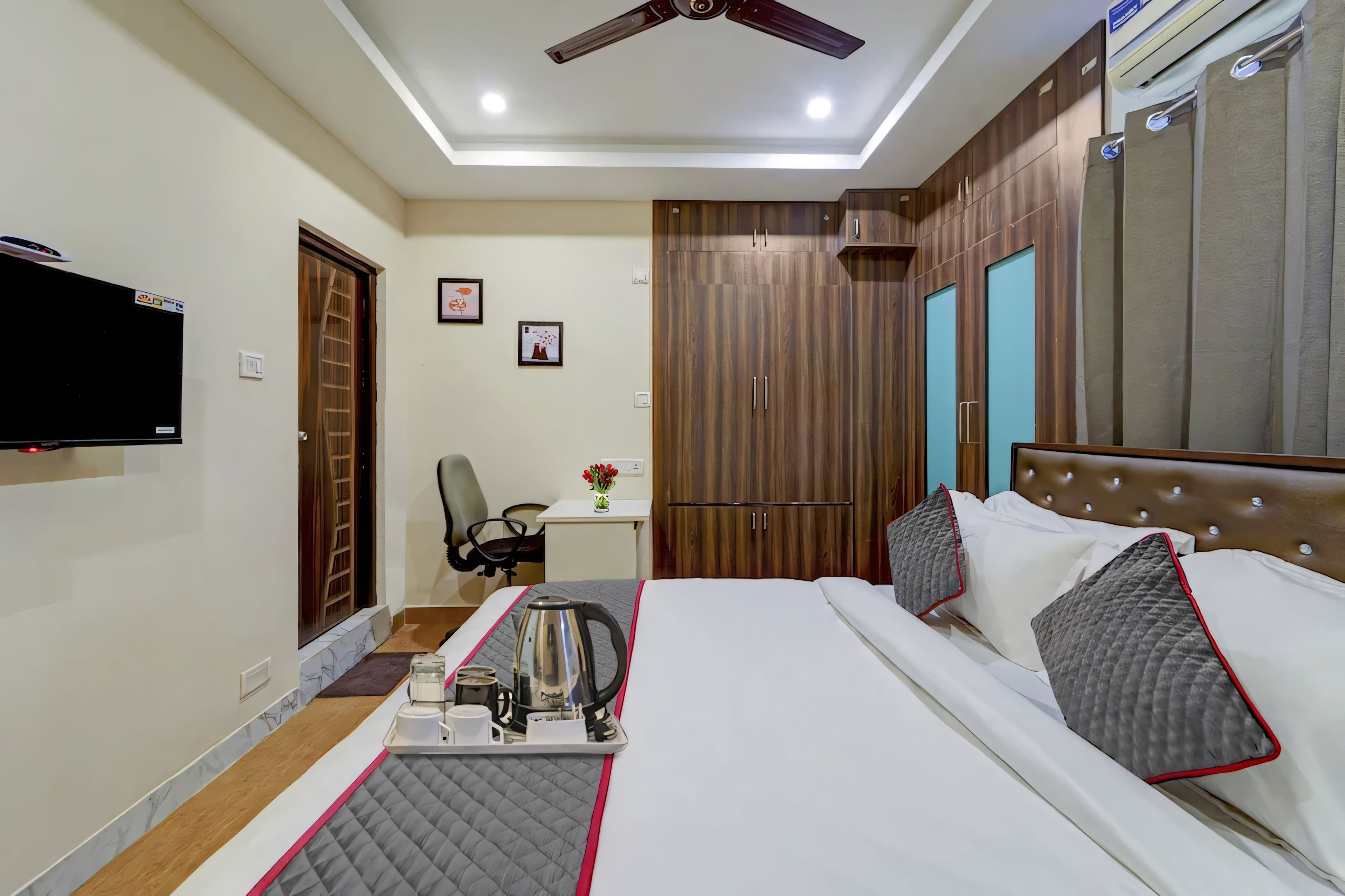 Habitación de hotel con cama, escritorio, silla, televisor y ventilador de techo.