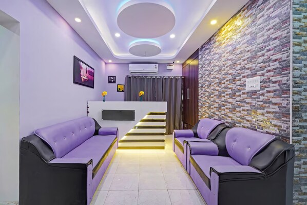 A modern interior with a reception desk, purple sofas, a staircase, and a patterned wall.