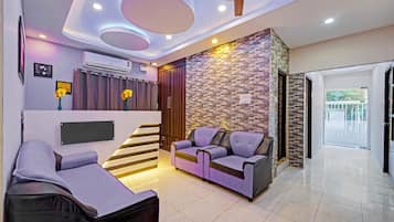 A modern living room with a sofa, a chair, a staircase, and a wall with a patterned design.