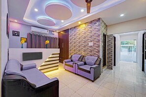 A modern living room with a sofa, a chair, a staircase, and a wall with a patterned design. - GSILVER HOTELS NUNGAMBAKKAM (Chennai)