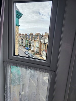 A window with a view of terraced houses and parked cars. - Happy Days Guesthouse (Bridlington)