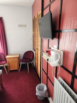 Una habitación pequeña con una televisión montada en la pared, una silla roja, un armario de madera y un radiador.