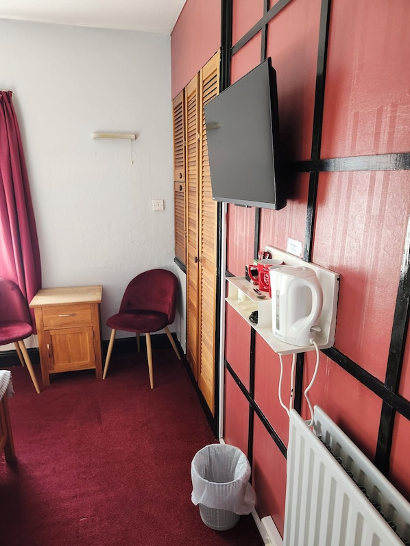 A small room with a television mounted on the wall, a red chair, a wooden cabinet, and a radiator.