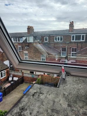 Vista a través de una ventana con edificios residenciales, cielo despejado y baranda metálica.