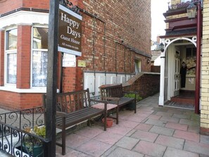A brick building with a sign reading 'Happy Days Guest House' and a bench outside. - Happy Days Guesthouse (Bridlington)