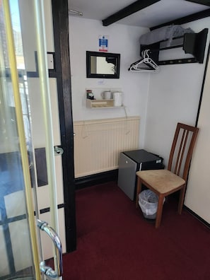A small room with a radiator, a desk, a chair, a hanging clothes rack, and a door with a glass panel. - Happy Days Guesthouse (Bridlington)