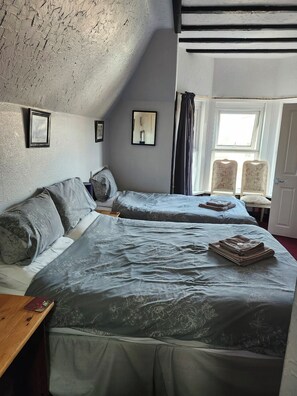A bedroom with two beds, a window with curtains, and a door.