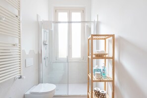 Een badkamer met een douchecabine van glas, een toilet en een houten plank met toiletartikelen.
