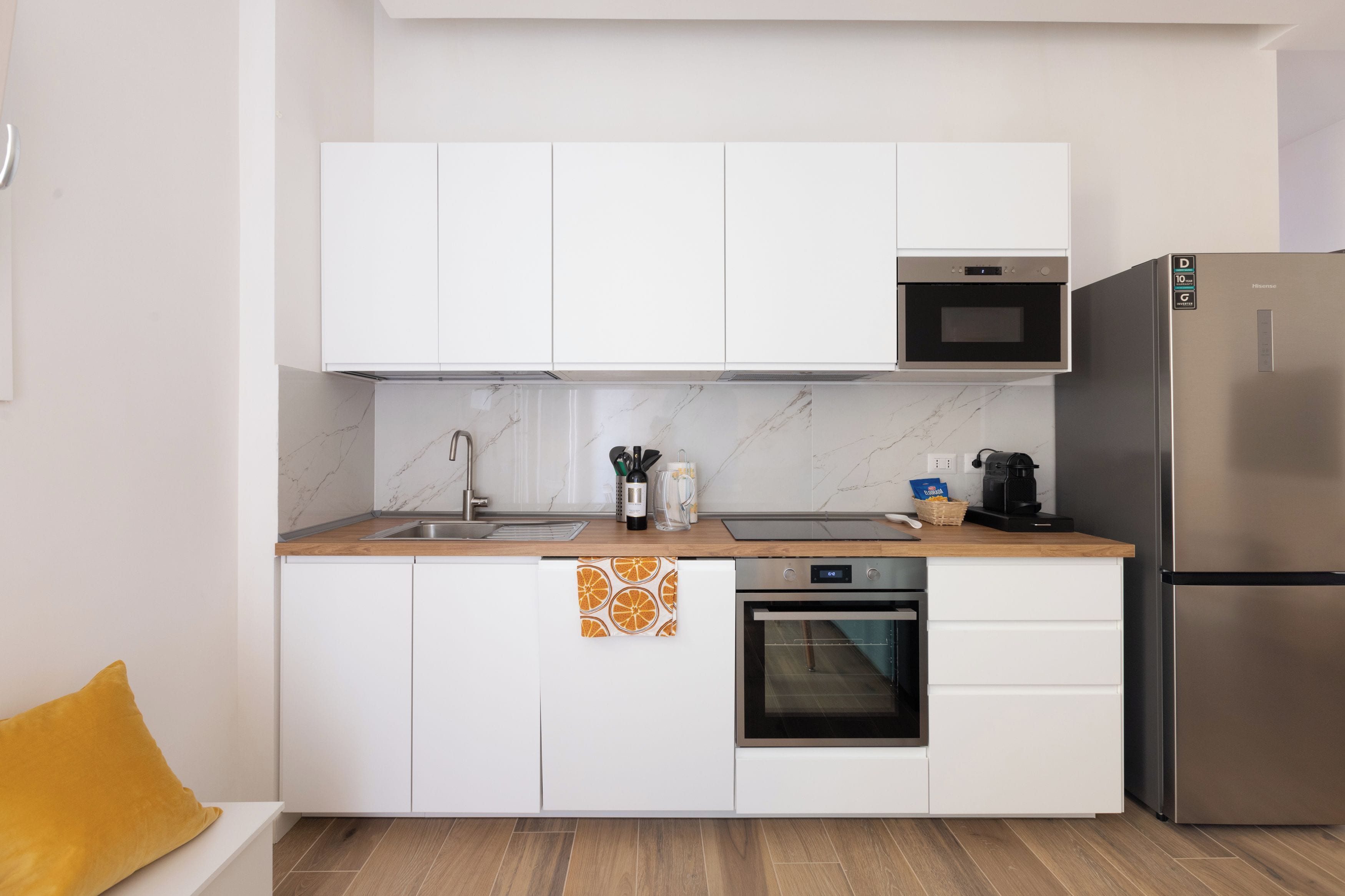 A modern kitchen with white cabinets, a stainless steel refrigerator, a microwave, and an oven.
