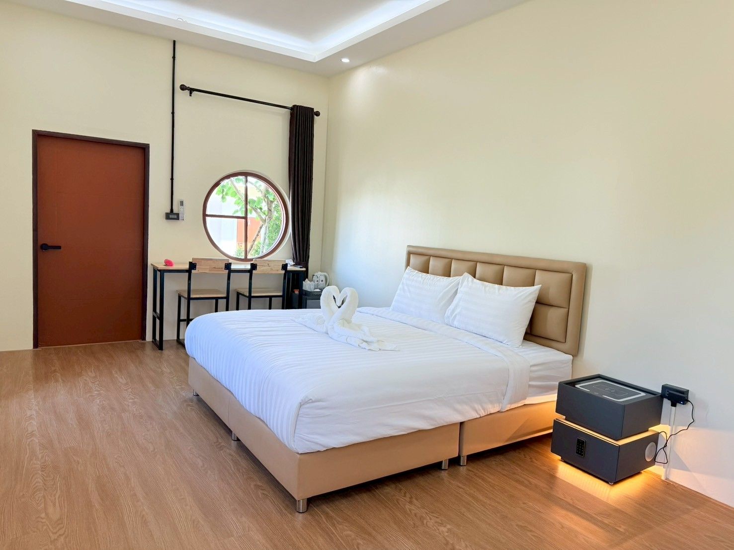 Quarto de hotel com cama, escrivaninha, cadeira, janela e porta.