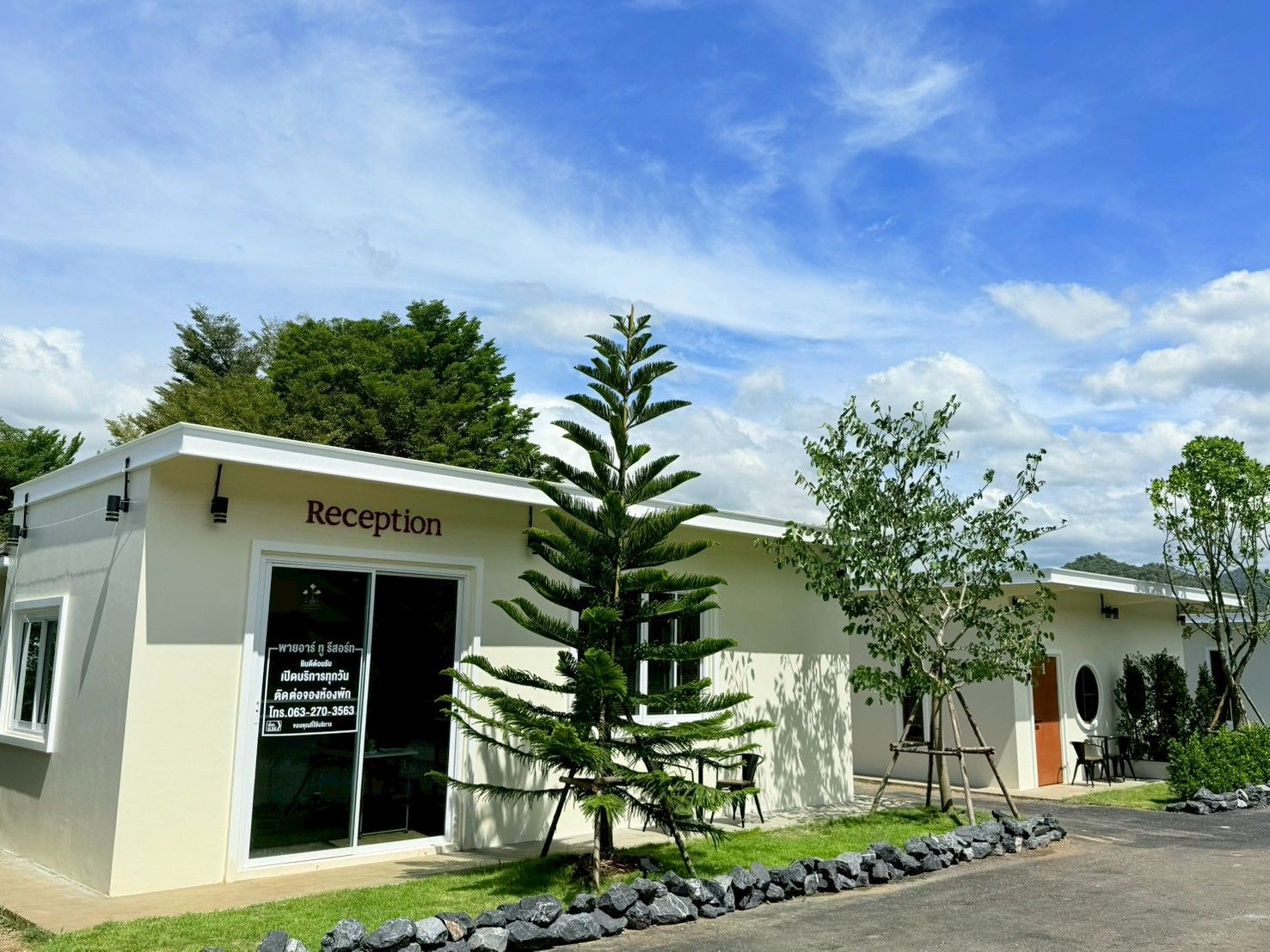 Edifício da recepção com uma placa, uma pequena árvore e um muro de pedra na frente.