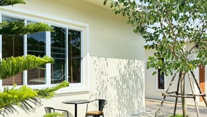 A modern outdoor seating area with a table and chairs, a small tree, and a building with large windows. - PiR 2 Resort 25 hours (Kaeng Khoi)