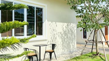 Uma área externa moderna com mesa e cadeiras, uma pequena árvore e um edifício com grandes janelas.