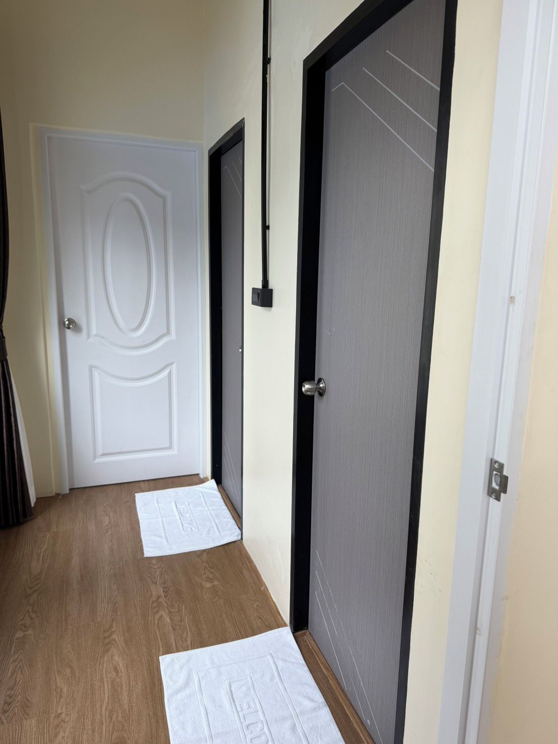 A hallway with a wooden floor, two doors, and a welcome mat.