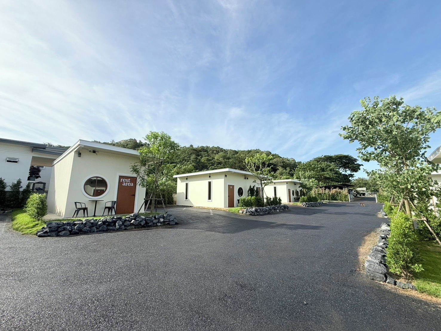 Zona residencial con camino de entrada pavimentado, un edificio pequeño identificado como 'rest area' y un sendero bordeado de árboles.
