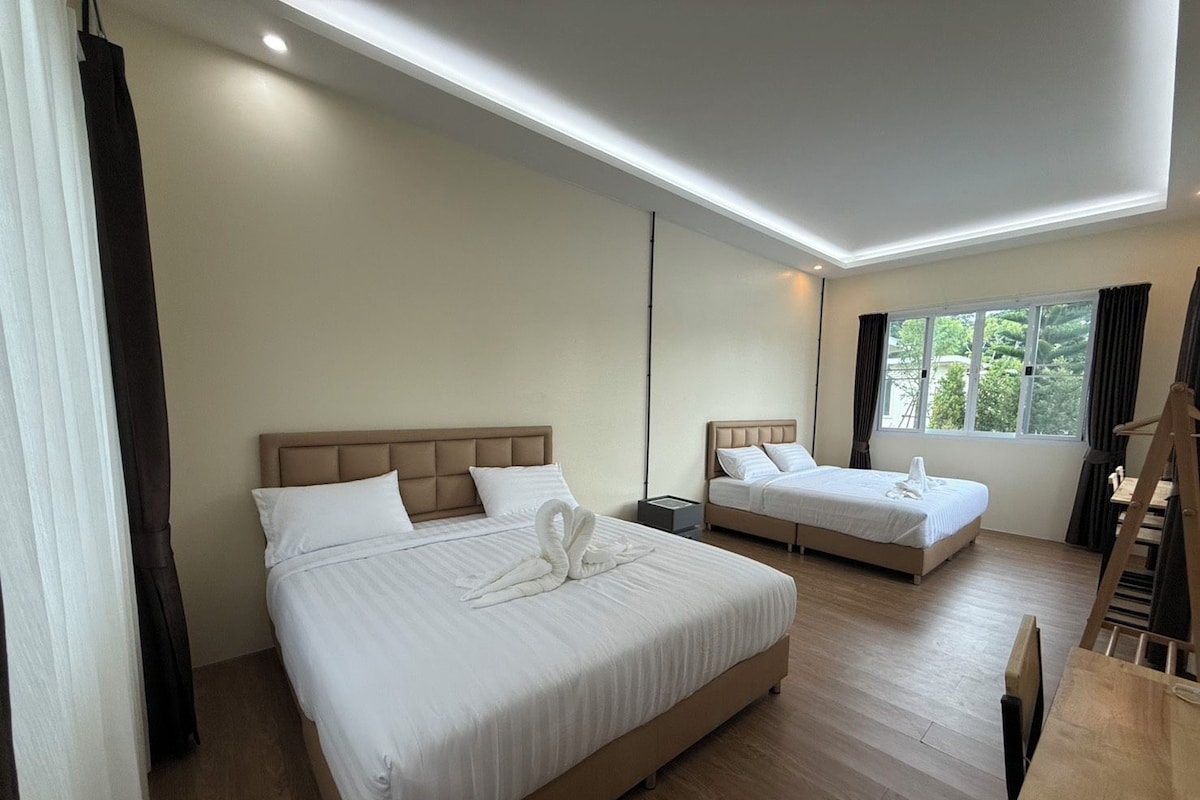 A hotel room with two beds, a wooden floor, a window with curtains, and a desk.