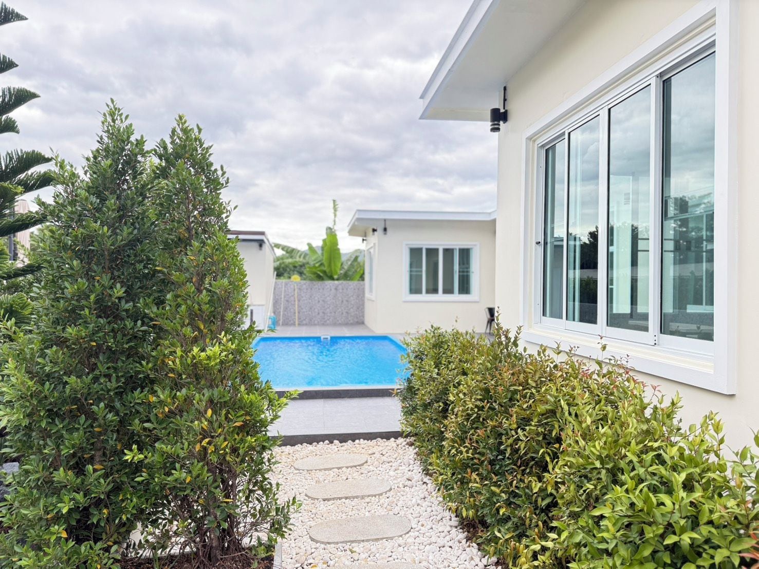 Um imóvel residencial com piscina, um caminho e uma casa com grandes janelas.