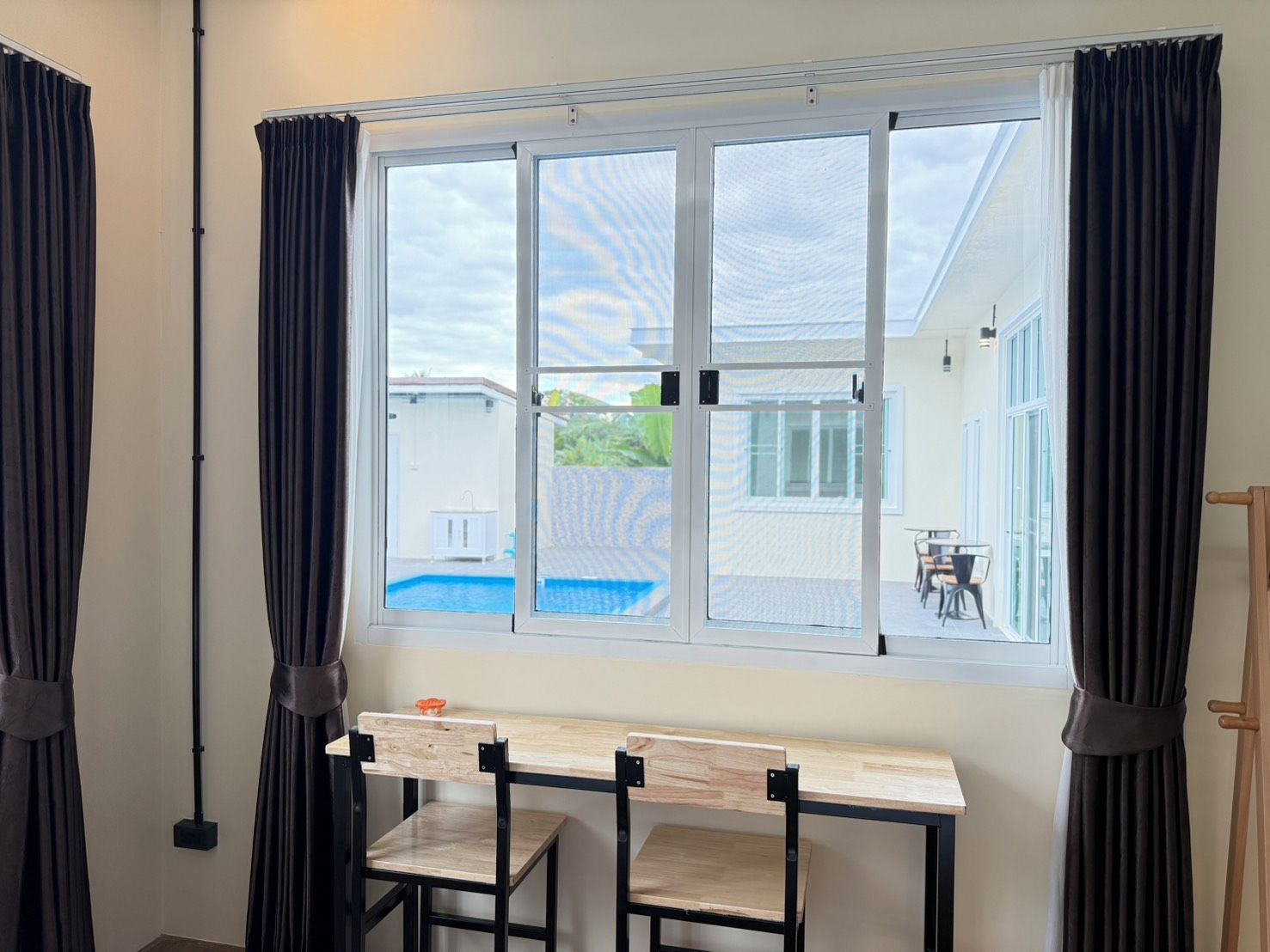 Una habitación con un ventanal grande, un escritorio, dos sillas y vistas a una piscina al aire libre.