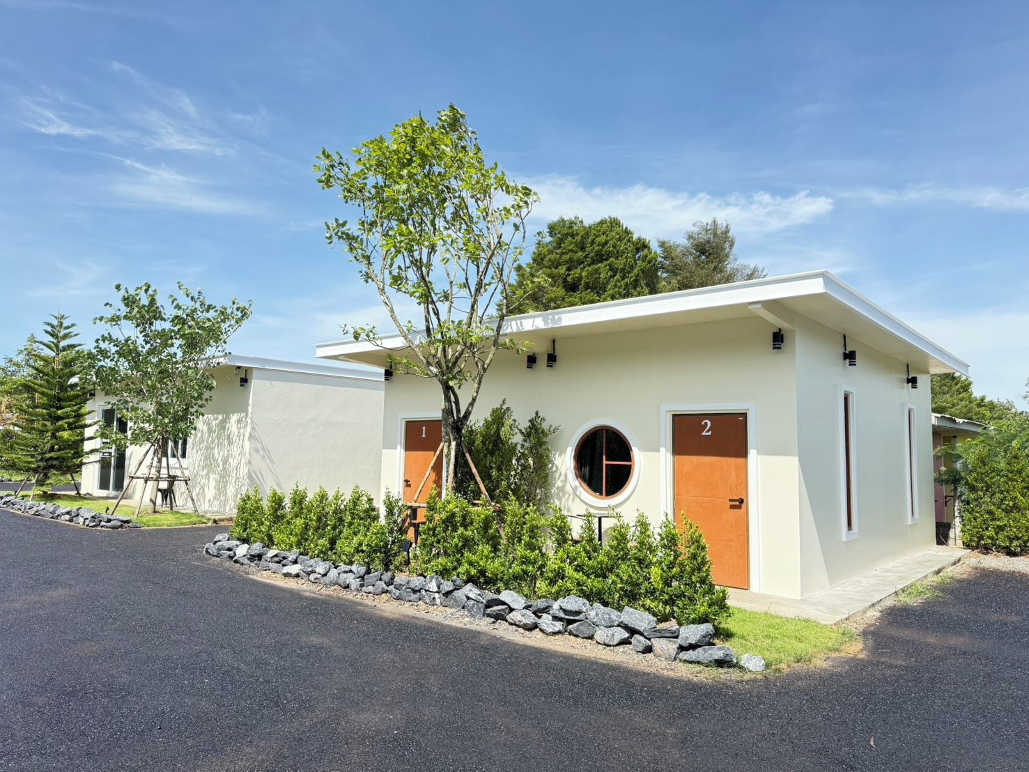 A modern two-story building with numbered doors, a circular window, and a tree in the front yard.