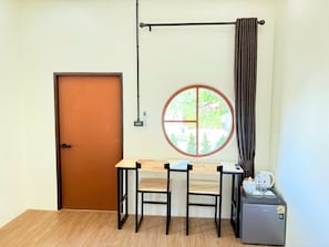 A room with a wooden door, a round window with a view, a table with chairs, and a small refrigerator.
