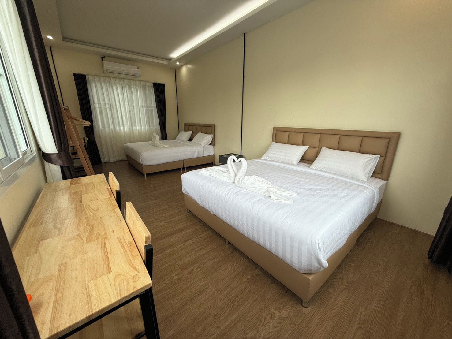 A hotel room with two beds, a wooden desk, and a window with curtains.