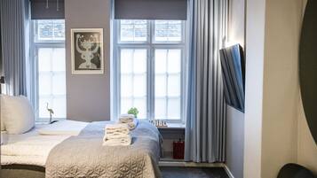A bedroom with two beds, a window with curtains, a wall-mounted TV, and a framed picture.