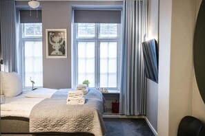 A bedroom with two beds, a window with curtains, a wall-mounted TV, and a framed picture. - Flat Near Copenhagen Canals (København)