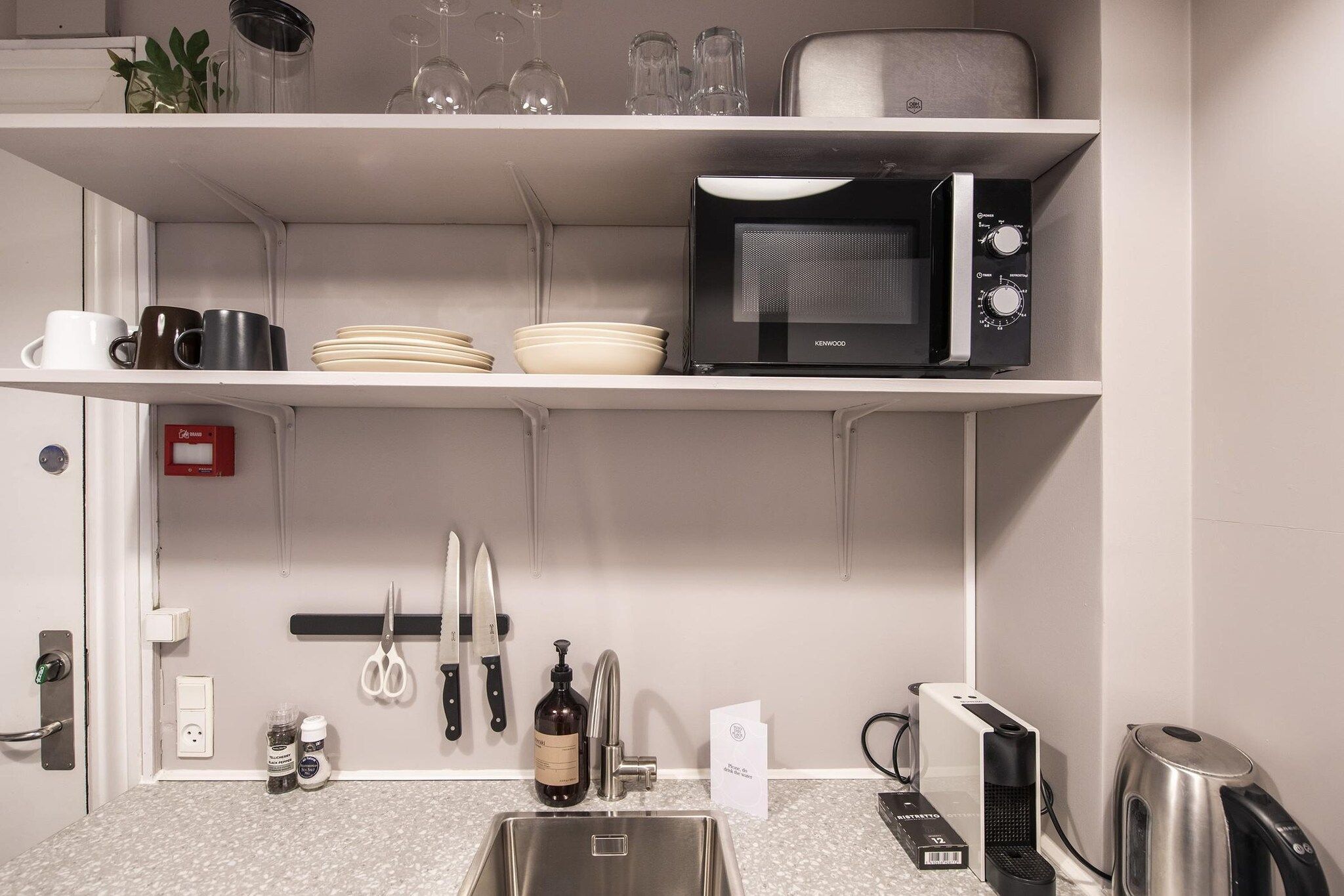 A kitchen with a microwave, sink, and various utensils.
