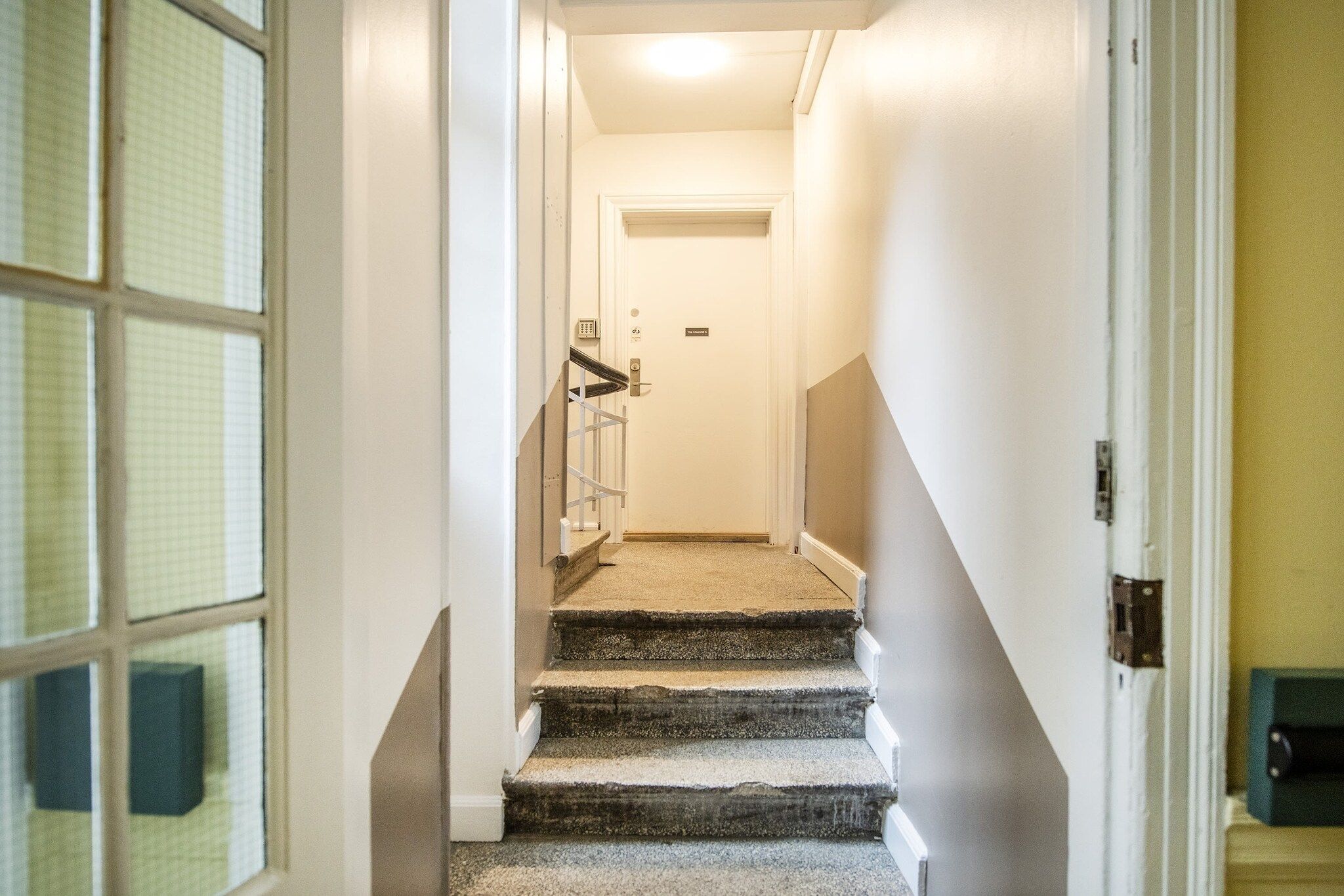 A carpeted staircase with a handrail, leading to a door with a keypad lock.